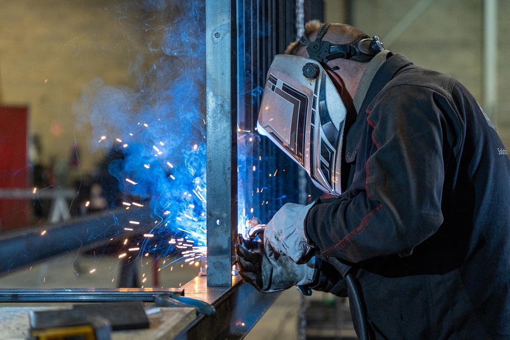 Soudeur avec masque de protection travaillant sur une structure métallique avec des étincelles bleues éclatantes.