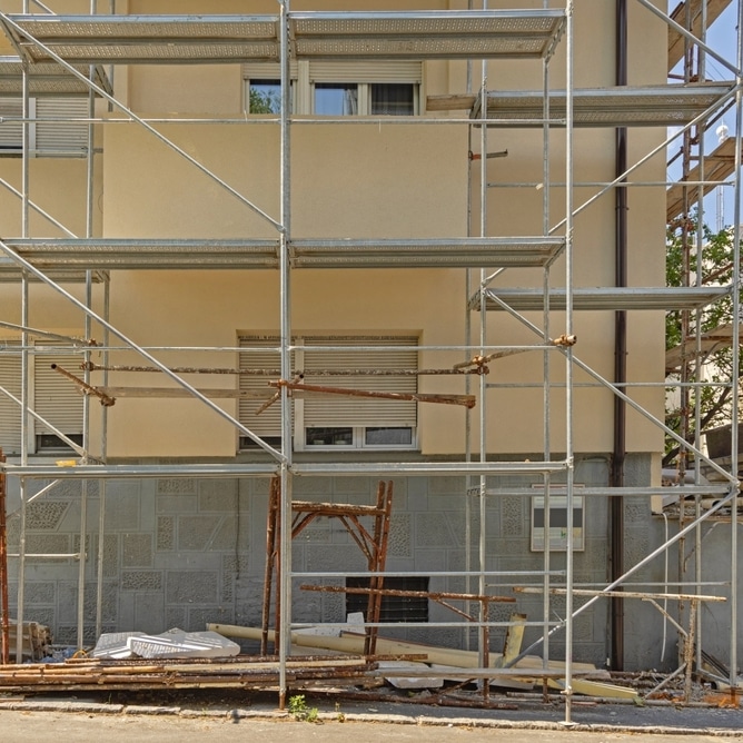 Échafaudage de Chantier pour Rénovation de Façade Échafaudage métallique devant une façade de bâtiment beige en cours de rénovation avec matériaux de chantier au sol.
