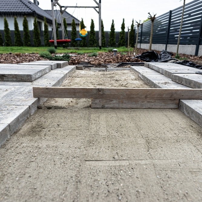 Pose de pavés de terrasse : étape du nivellement du sable Nivellement du sable avec des planches pour la pose de pavés de terrasse dans un jardin avec balançoire.